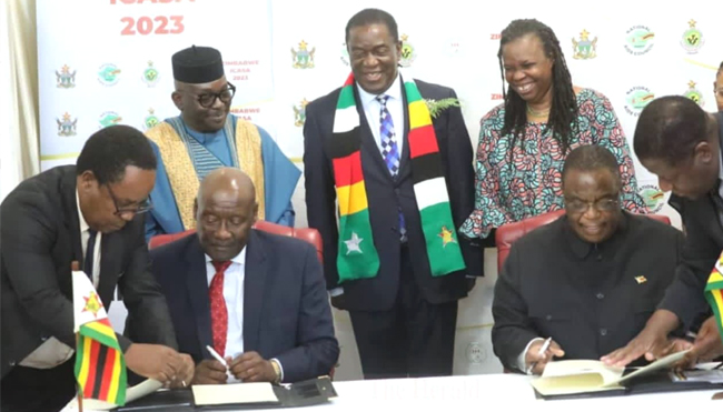 From left(Front): Dr. Bernard Madzima, CEO of NAC assisting Hon. Dr. David Pagwesese Parirenyatwa, SAA/ICASA 2023 President, with H.E. Dr. C. G.D.N. Chiwenga, Vice President and Minister of Health and Childcare/ICASA 2023 Vice President, Zimbabwe, being assisted by Air Commodore (Dr.) Jasper Chimedza, Permanent Secretary for Ministry of Health and Child Care, at the signing of the MoU at State House, Harare, Zimbabwe In the background, From left: Mr. Luc Armand Bodea, ICASA Director, H.E. Emerson Mnangagwa, President of. Zimbabwe, Prof. Morenike Ukpong, SAA Treasurer and Dr. Fikile Ndlovu, SAA Deputy Secretary General, during the Signing of the ICASA 2023 MoU, State House, Harare, Zimbabwe